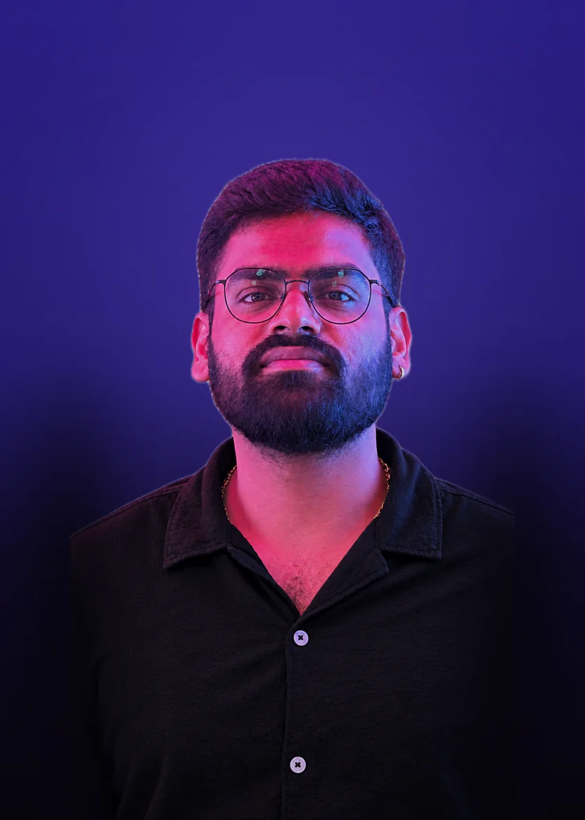 Anuj Patel in a dark shirt and glasses, lit pink and blue, against a violet backdrop